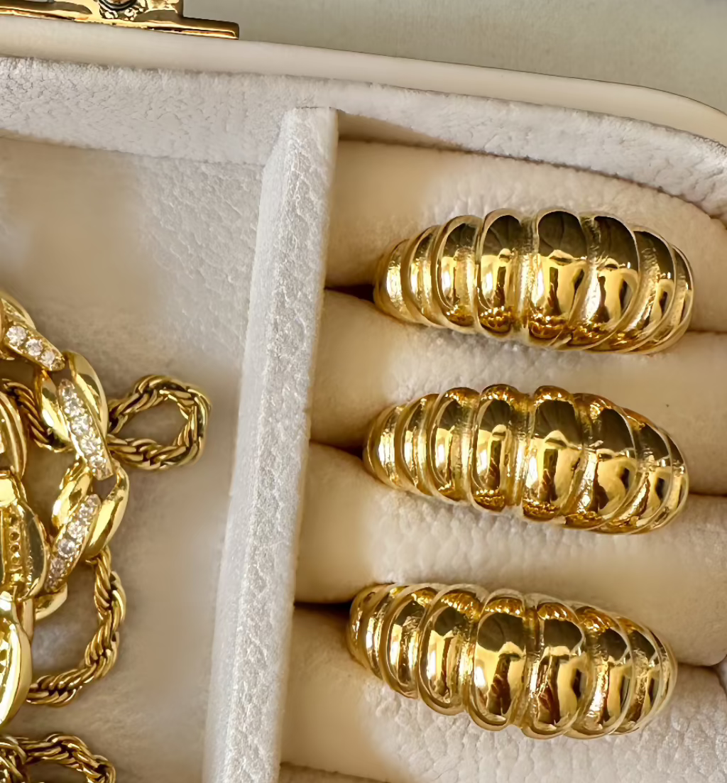 A close-up image of a gold croissant ring with a ribbed dome design, displayed in a jewelry box.
