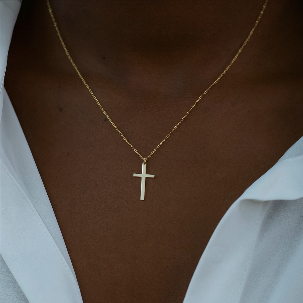 Gold necklace with a cross pendant on a person wearing a white shirt.