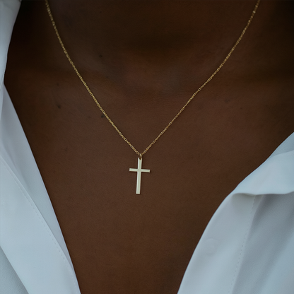 Gold necklace with a cross pendant on a person wearing a white shirt.