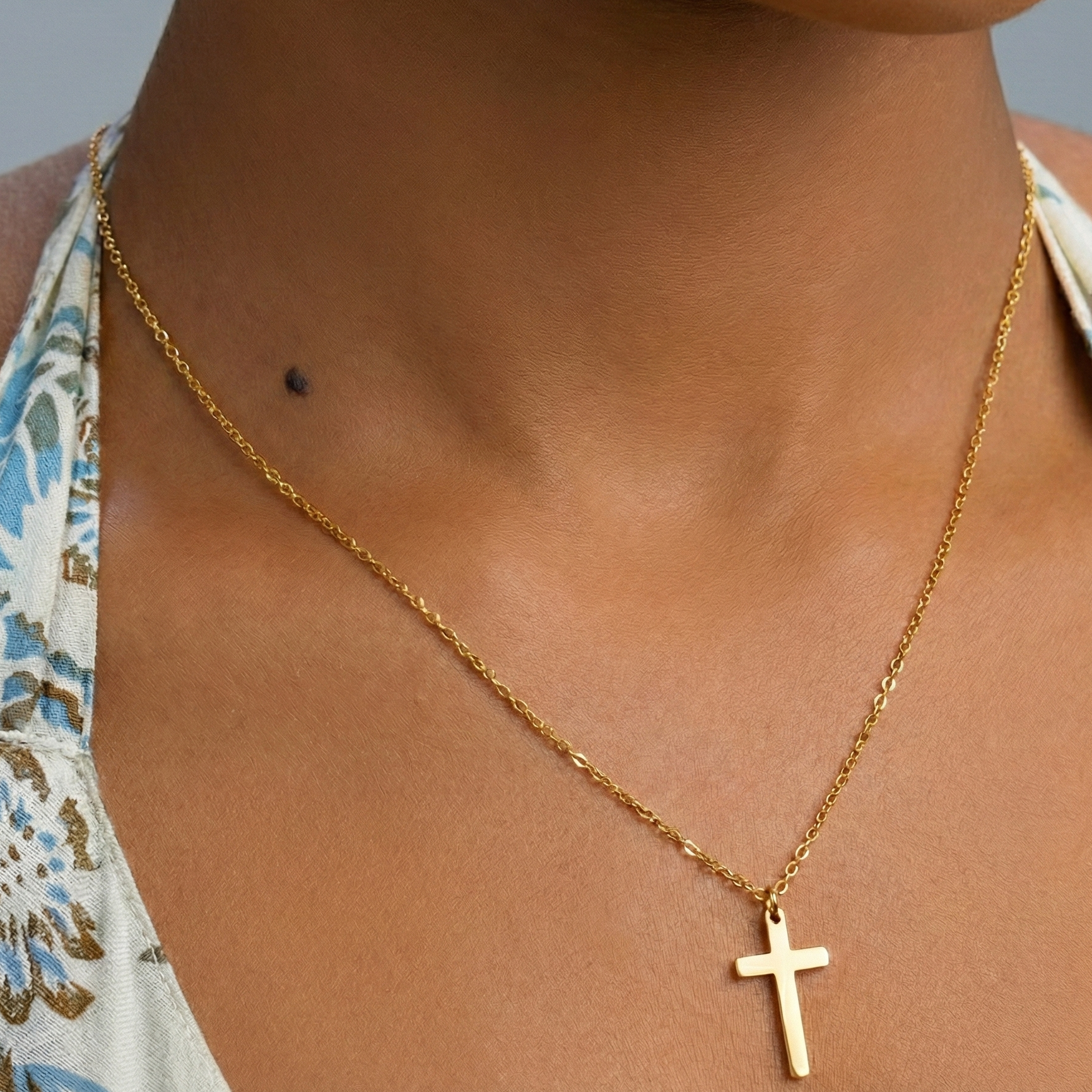 Gold necklace with a cross pendant on a person wearing a floral top.